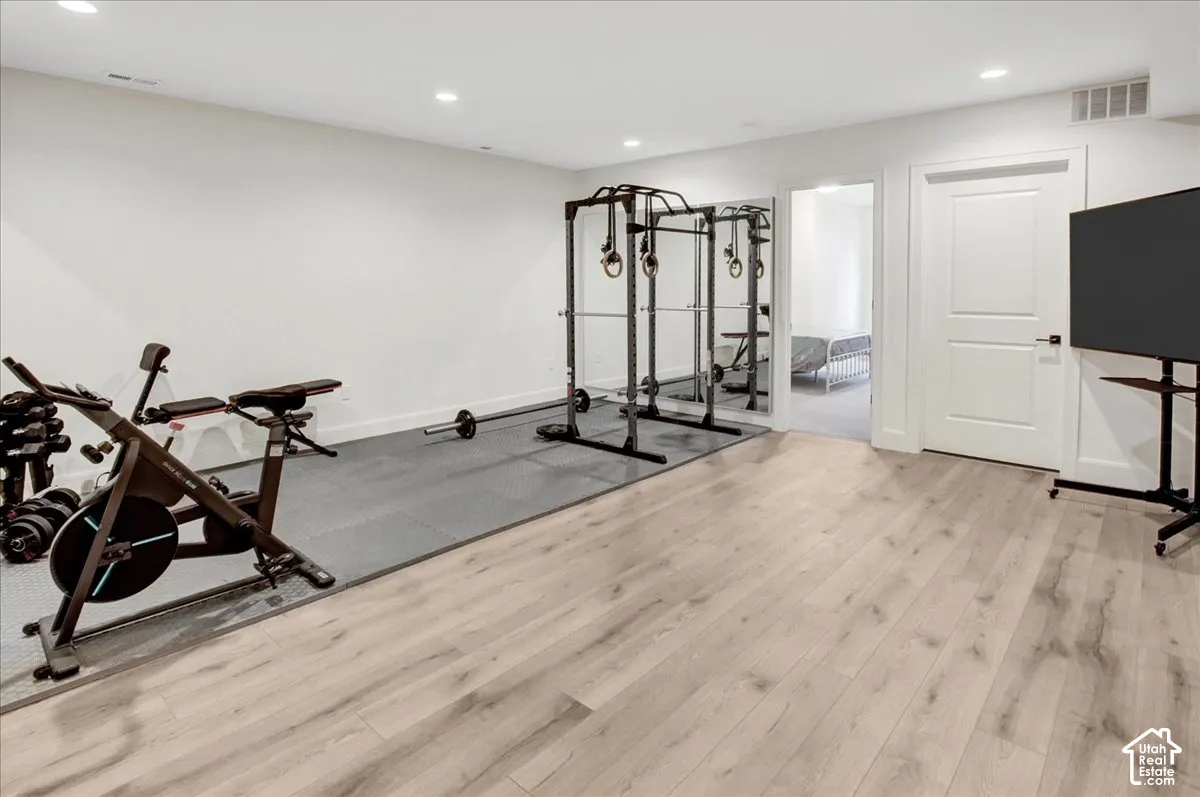 Light wood-finish flooring, recessed lighting, white interior door, and a dedicated exercise area with protective matting