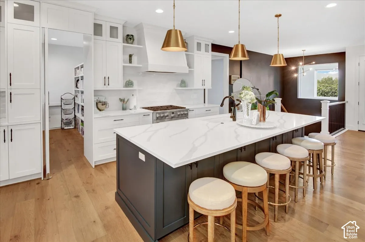 Gourmet kitchen with white cabinetry, a large center island with a light-toned countertop, wood-finish flooring, and integrated stainless steel appliances