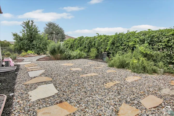 Landscaped exterior featuring a stone paver pathway, gravel ground cover, and a lush green privacy hedge