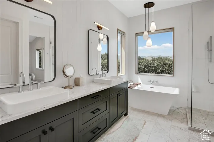 Dual vanity with vessel sinks, a freestanding soaking tub, a walk-in shower with glass enclosure, and a multi-pendant light fixture