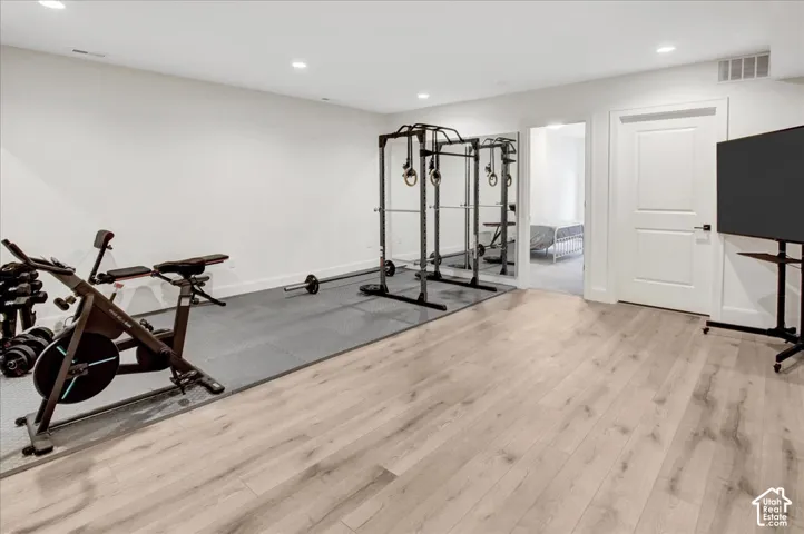 Light wood-finish flooring, recessed lighting, white interior door, and a dedicated exercise area with protective matting