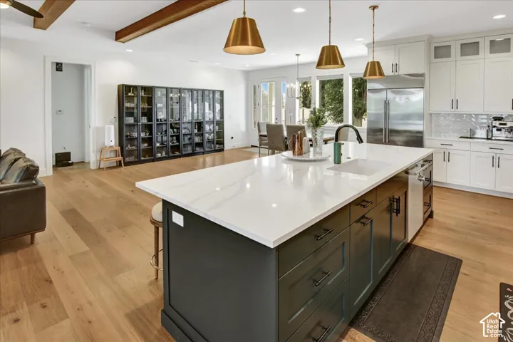 Kitchen featuring a large island with a white countertop and dark cabinetry, white upper and lower cabinetry, stainless steel appliances, and wood-finish flooring