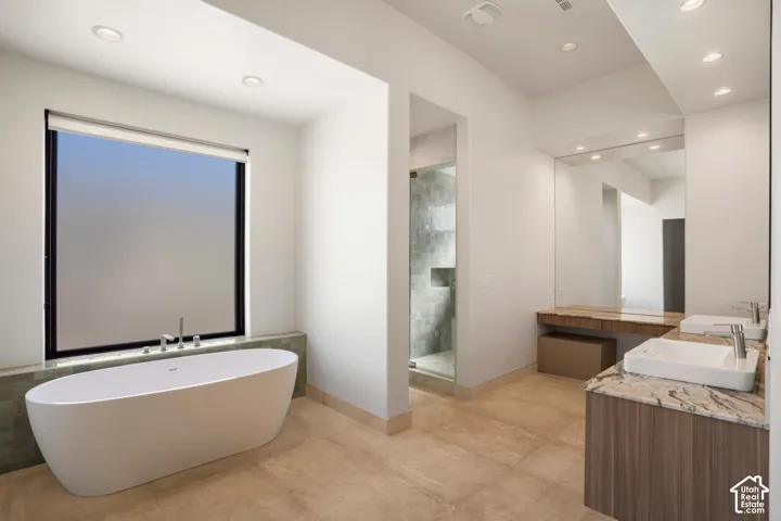 Freestanding soaking tub with a deck-mounted faucet, vanity with dual rectangular vessel sinks, stone-surface countertop, full-width mirror, and walk-in glass-enclosed shower