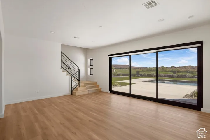 Wood-finish flooring, recessed lighting, staircase with black metal railing, and multi-panel sliding glass doors