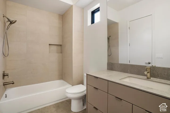 Bathroom featuring a vanity with a stone countertop, a wall-to-wall mirror, a soaking tub with an integrated shower niche, and floor-to-ceiling tile surround