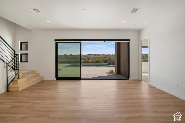 Open-concept living space featuring wood-finish flooring, recessed lighting, floor-to-ceiling sliding glass doors, a staircase with metal railings, and a concrete patio with a swimming pool