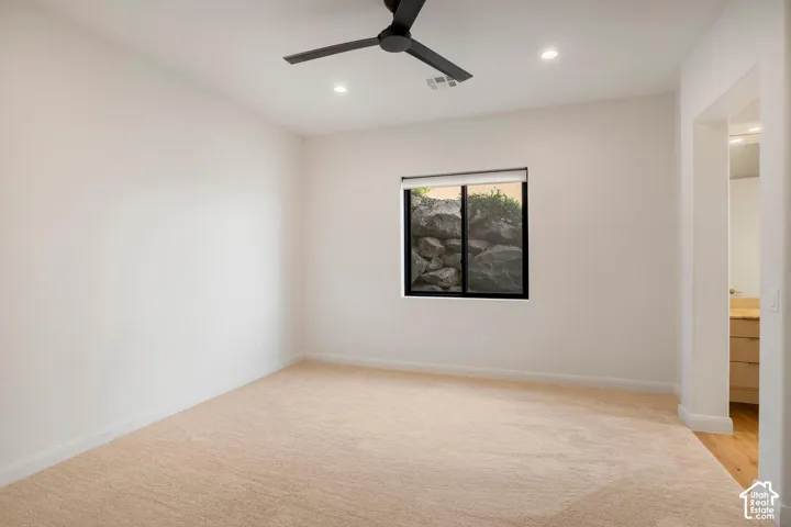 Neutral-toned carpeting, recessed lighting, matte black ceiling fan, and slider window with exterior natural rock feature