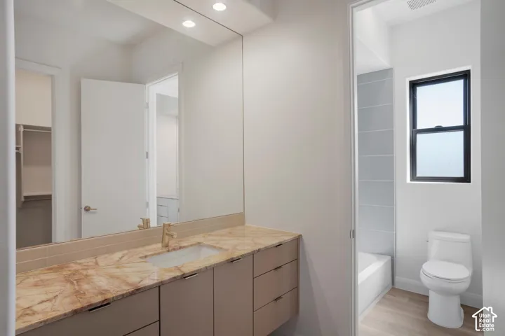 Floating vanity with a stone countertop, integrated rectangular sink, metallic faucet, full-width mirror, and wood-finish flooring