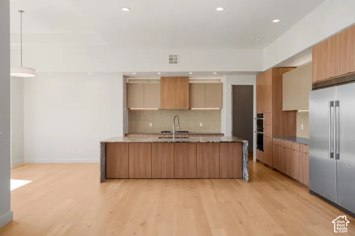 Kitchen featuring wood-finish cabinetry, stone-top island with waterfall edge, integrated stainless steel appliances, and wood-finish flooring