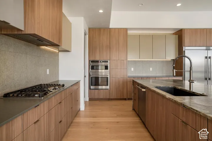 Modern kitchen featuring full-height wood-finish cabinetry, a large central island with a stone-finish countertop, integrated stainless steel double wall ovens, a gas cooktop, and recessed lighting