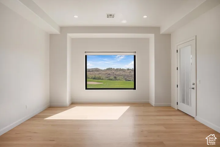 Room featuring wood-finish flooring, a tray ceiling with recessed lighting, and a frosted glass door, showcasing a large picture window with mountain and green space scenery