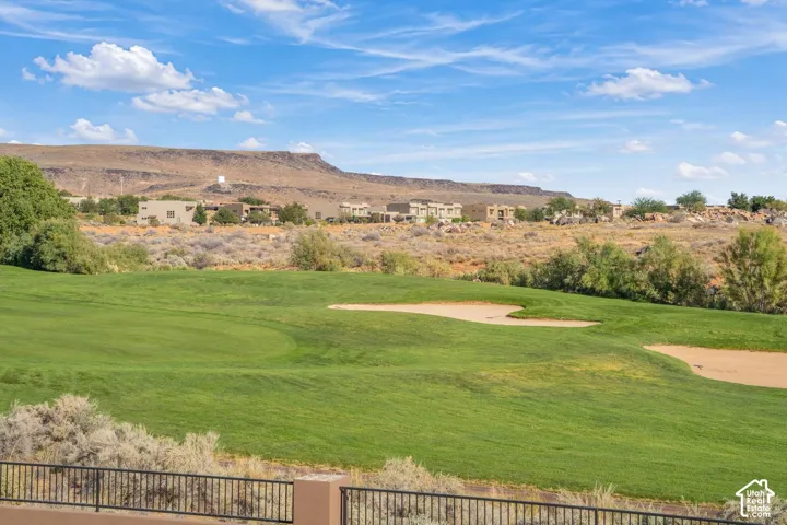 Expansive green space featuring sand bunkers, mature native vegetation, and a metal perimeter fence, set against a backdrop of desert mesas