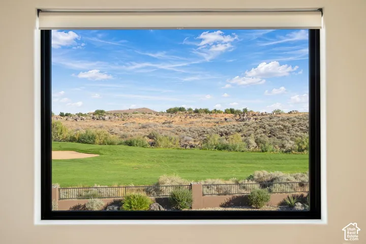 Large picture window with a black frame and retractable roller shade, framing a landscape of desert terrain and open grass