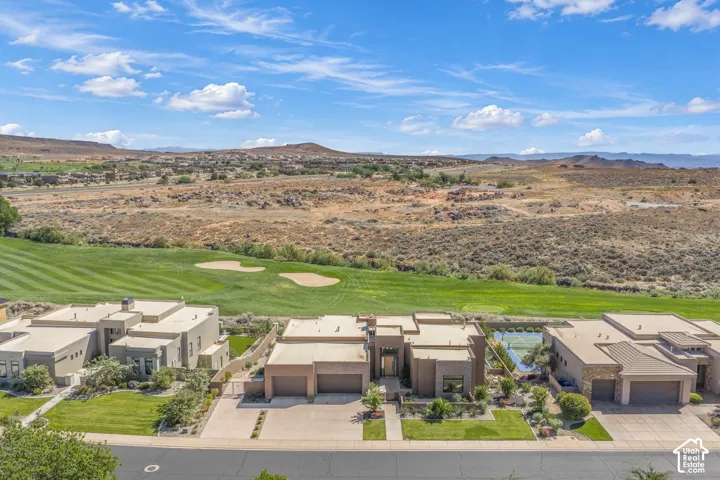 Aerial perspective of stucco exterior residence featuring a multi-car garage, private tennis court, and immediate proximity to a golf course