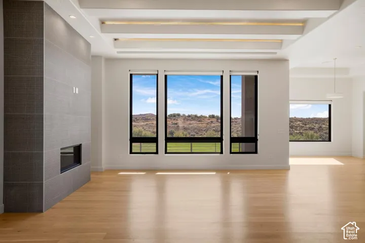 Living area featuring light-toned wood-finish flooring, a full-height tiled fireplace surround, recessed ceiling lighting, and expansive windows with desert landscape scenery