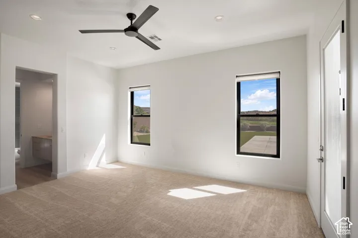 Neutral-toned carpeting, matte black ceiling fan, recessed lighting, expansive windows with black frames, and glass-paneled exterior door
