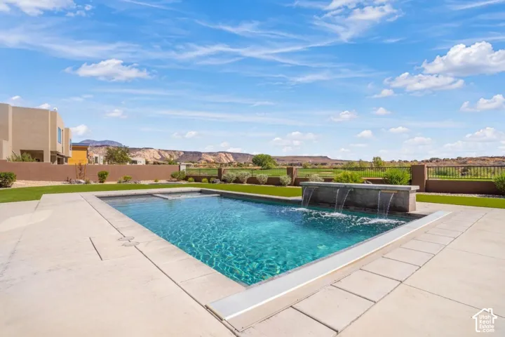 In-ground swimming pool featuring a built-in water feature and concrete deck, accompanied by a landscaped lawn and stone boundary wall