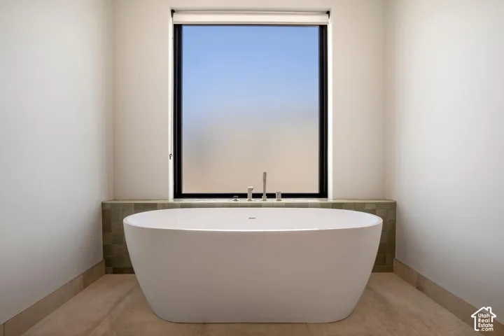 Freestanding white soaking tub with deck-mounted fixtures, set against a tiled back-splash and a large window with a black frame
