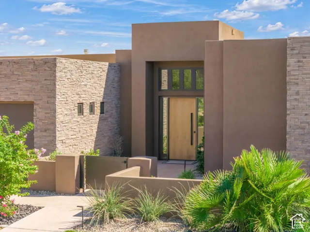 Contemporary exterior featuring smooth stucco finish, textured stone masonry accents, a natural wood-finish front door with an elongated vertical pull, and integrated transom windows
