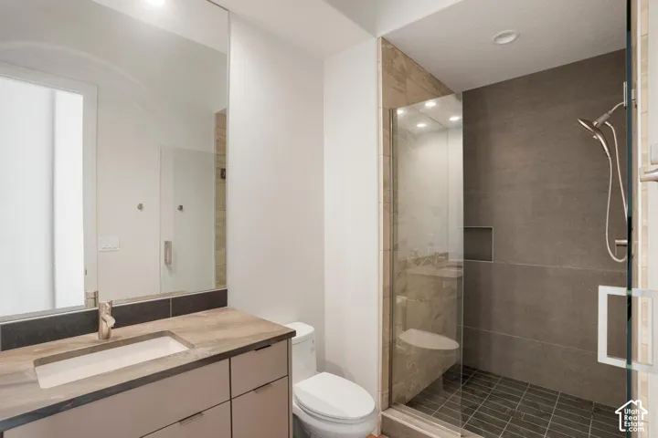 Bathroom featuring a vanity with a rectangular sink and stone-finish countertop, a large wall-mounted mirror, and a walk-in shower with a glass enclosure, built-in shelving, and neutral-toned tile surrounds