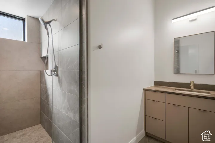 Bathroom featuring a walk-in shower with large-format tile surround, hand-held shower fixture, vanity with solid-surface countertop, and integrated linear lighting
