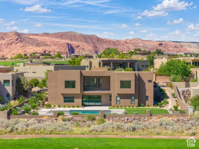 Modern two-story architectural exterior featuring smooth stucco siding, large glass windows, a private pool, and a fenced rear yard with mountain scenery
