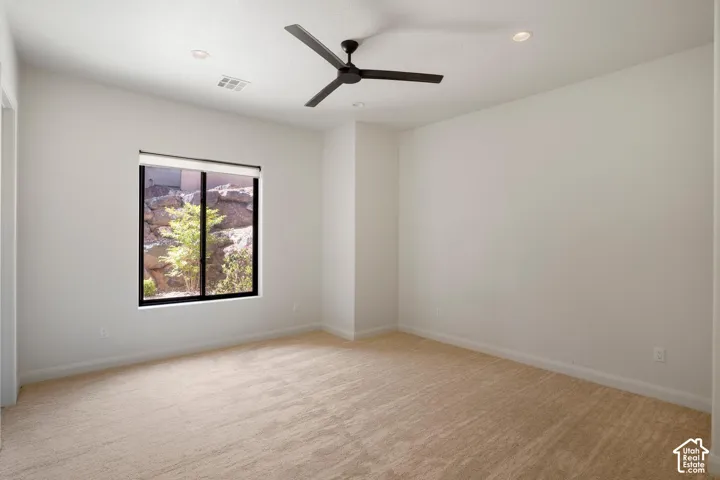 Neutral-toned interior space featuring recessed ceiling lighting, a three-blade matte black ceiling fan, wall-to-wall carpeting, and a window with a rock landscape backdrop