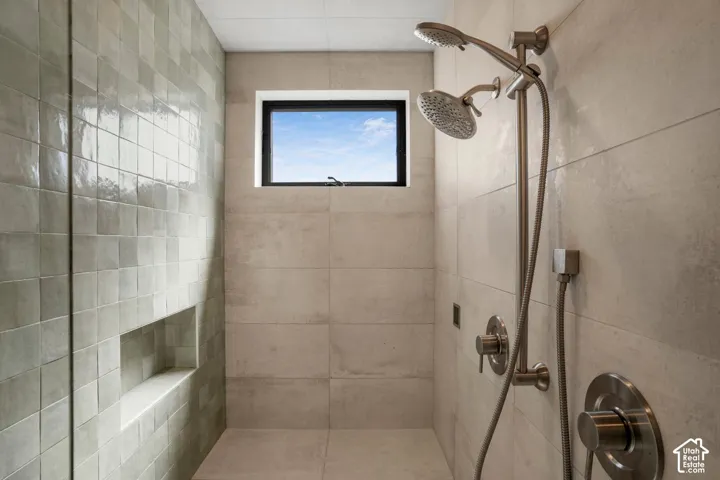 Walk-in shower featuring large-format stone-finish wall tile, an accent wall of textured square tiles, a recessed wall niche, a dual-head shower system with brushed metal finish, and a rectangular window