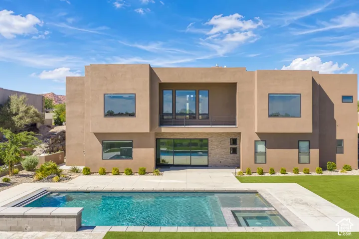 Contemporary two-story exterior featuring a smooth stucco finish, stone masonry accents, a second-story balcony with cable railing, large picture windows, and a rectangular swimming pool with a spillover spa