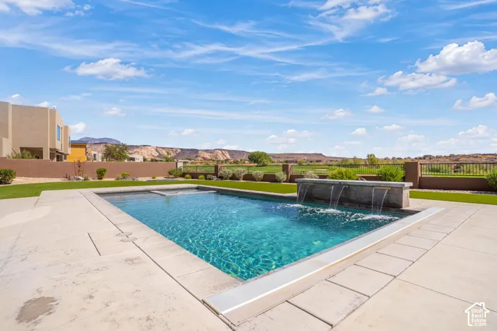In-ground pool featuring a raised stone water feature, integrated spillway, concrete decking, and perimeter fencing