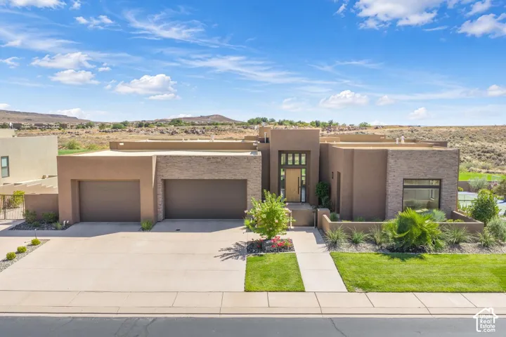 Contemporary stucco exterior featuring stacked stone accents, a three-car garage, and a modern recessed entry with floor-to-ceiling glass paneling