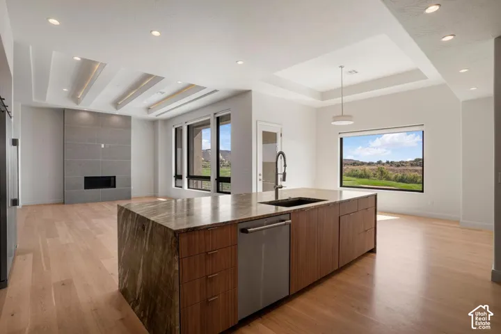 Kitchen featuring a stone-topped island with wood cabinetry, recessed ceiling lighting, wood-finish flooring, a tray ceiling, and a fireplace with stone surround