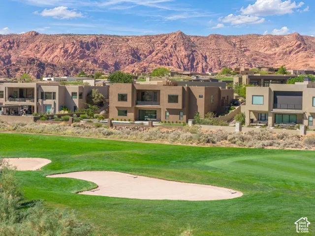 Exterior featuring contemporary multi-story architecture, manicured golf course frontage, sand bunkers, and a prominent red rock mountain backdrop