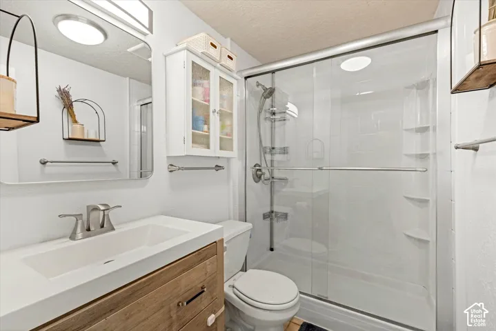 Bathroom featuring a wood-finish vanity with a rectangular integrated sink, wall-mounted white cabinetry, a glass-enclosed shower with a hand-held sprayer, and a polished vanity mirror with integrated lighting