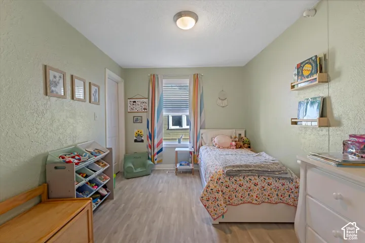 Neutral-toned room featuring wood-finish flooring, a single-pane window with interior blinds, and wall-mounted shelving