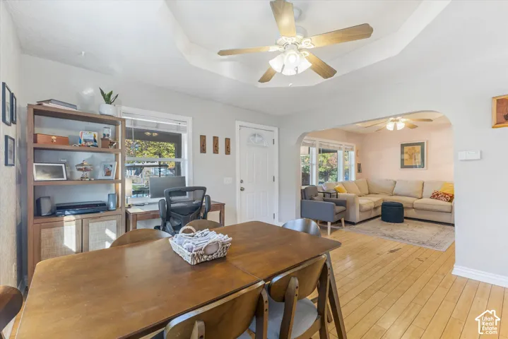 Tray ceiling with a central multi-blade ceiling fan, light wood-finish flooring, and arched architectural opening