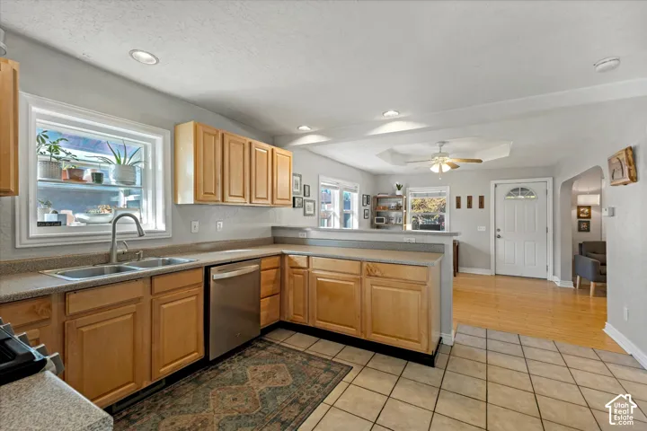 Kitchen featuring light-tone wood cabinetry, stainless steel dishwasher, dual-basin stainless steel sink with pull-down faucet, and neutral tile flooring