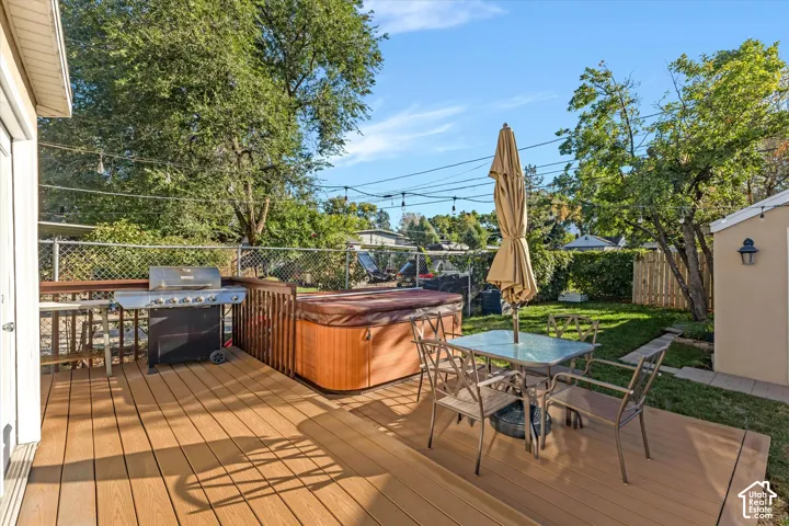 Raised wooden deck featuring an integrated hot tub and string lighting, complete with a private backyard, manicured lawn, and mature trees