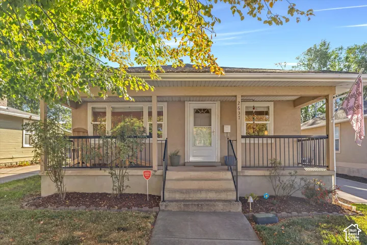 Stucco exterior featuring a covered front porch with black metal railings, concrete steps, and multi-pane windows
