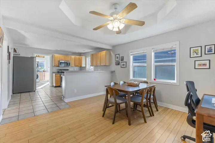 Tray ceiling featuring a central light fixture and ceiling fan, wood-finish flooring, ceramic tile kitchen flooring, and light-toned wood cabinetry