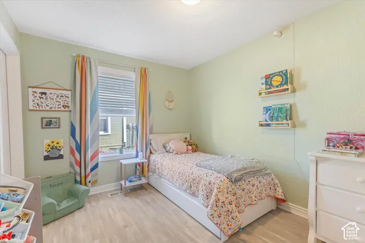 Room featuring light-toned wood-finish flooring, a single-pane window, and two wall-mounted floating wood shelves