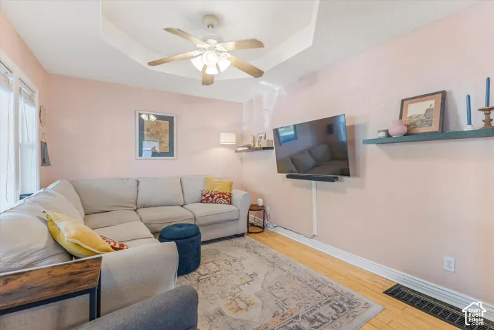 Tray ceiling with a central multi-blade ceiling fan, wood-finish flooring, and built-in wall shelving