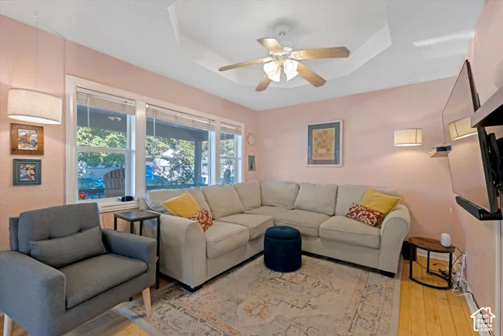 Living area featuring a tray ceiling, wood-finish flooring, and a central ceiling fan with integrated lighting