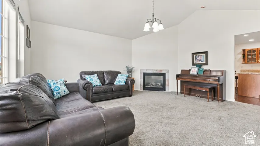 Vaulted ceilings, carpeted flooring, built-in fireplace with tile surround, and an overhead chandelier fixture