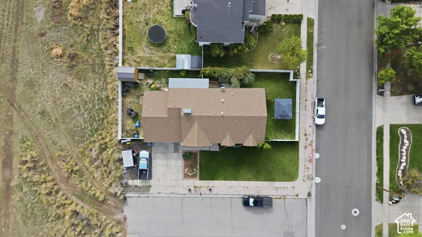 Aerial perspective of a corner lot property featuring a fenced backyard, multi-pitched shingle roof, concrete driveway, and front lawn