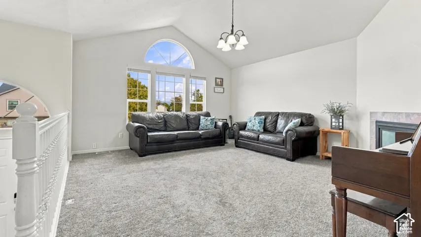 Vaulted ceiling with a five-light chandelier, arched window, carpeted flooring, and a fireplace with a stone-surround hearth