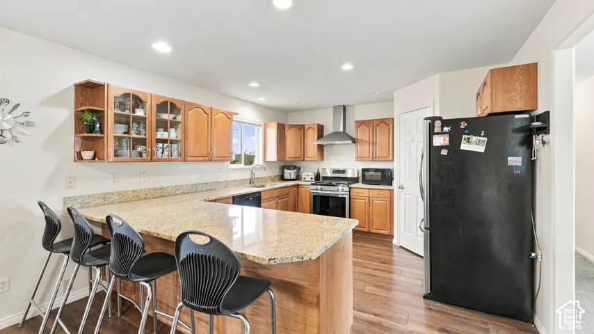 Kitchen featuring wood cabinetry, stone countertops, breakfast bar, recessed lighting, and stainless steel range hood