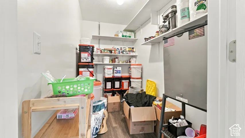Storage area featuring multiple tiers of wall-mounted shelving and wood-finish flooring