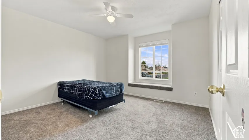 Carpeted interior featuring a built-in window seat, grid-patterned window, ceiling fan with integrated lighting, and a six-panel interior door