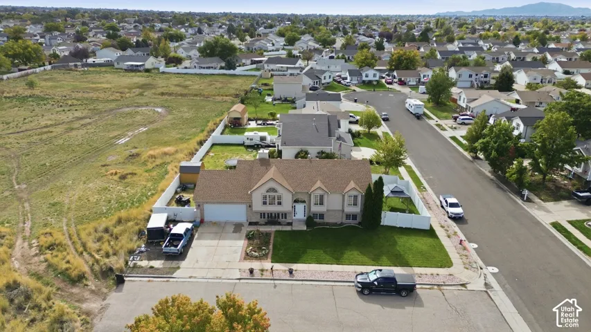 Aerial perspective of a multi-level residence featuring a pitched shingle roof, attached two-car garage, manicured front lawn, and perimeter vinyl fencing